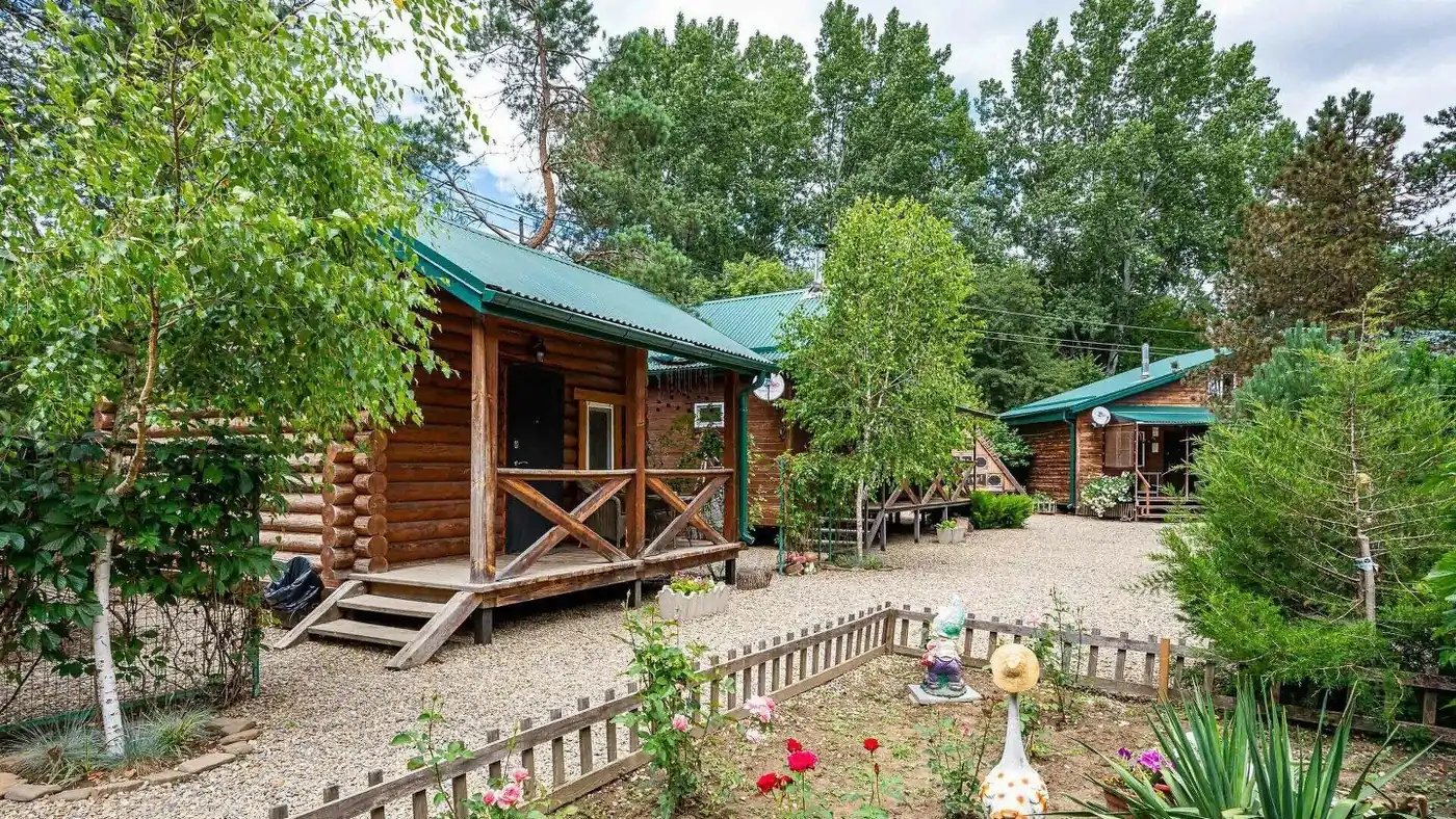 Бревенчатый домик с зелёной крышей и садовыми фигурками во дворе